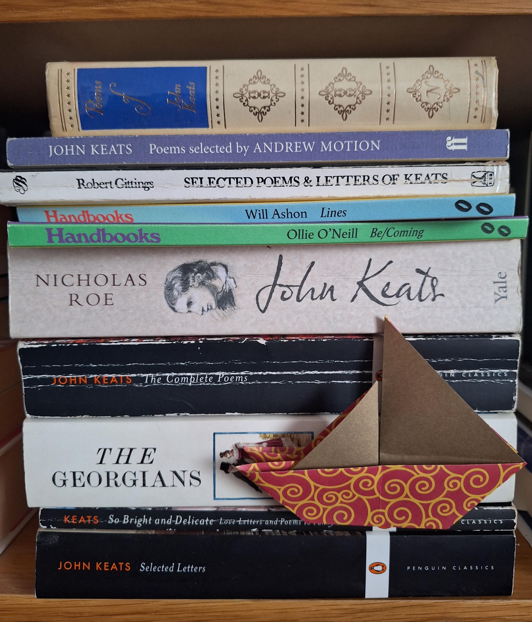 A pile of books - various copies of Keats' poems interspersed with two Blown Rose Handbooks - and a small origami sailing boat tucked in.
